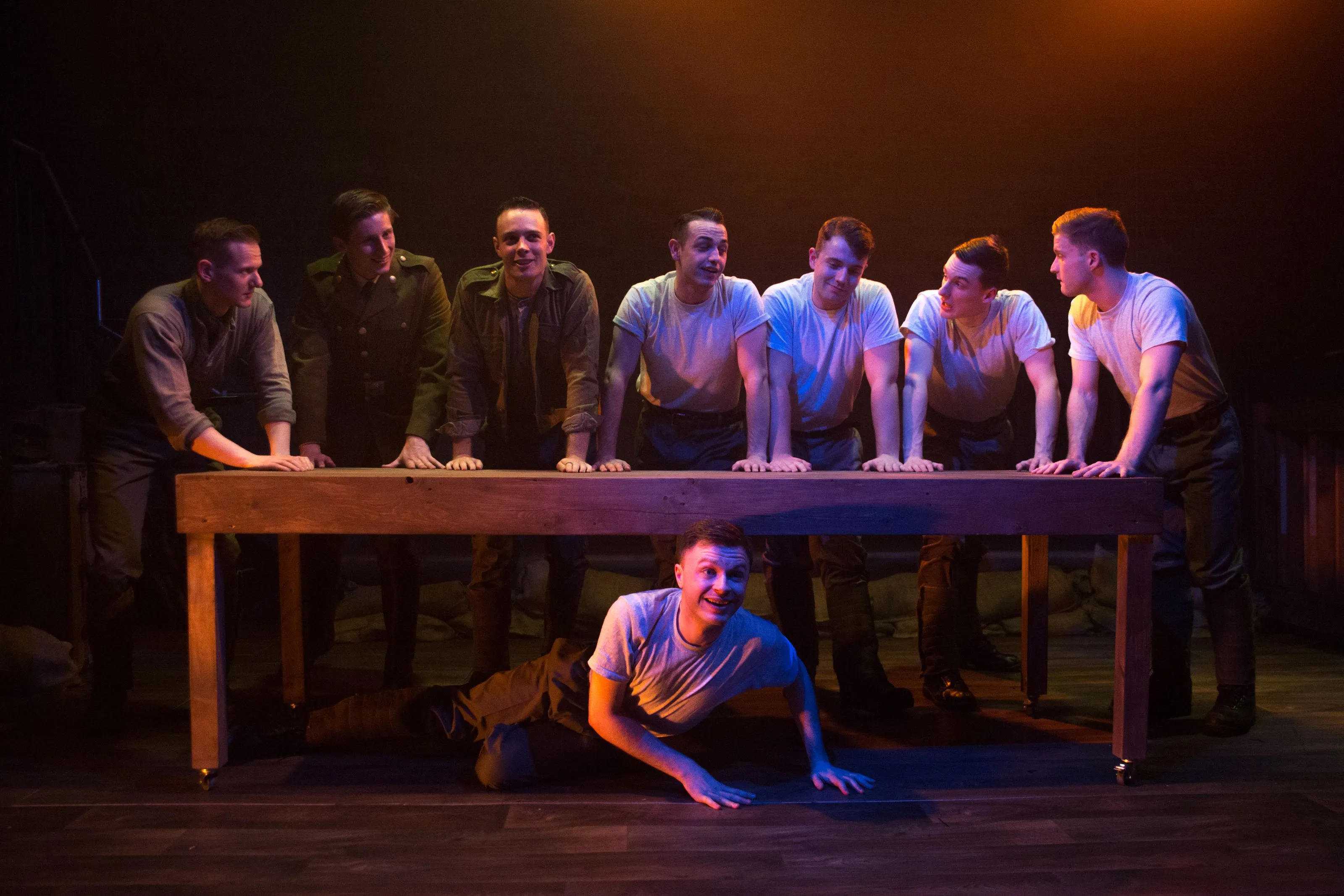 Military men stand at a long table smiling in a warm mix of orange and purple light