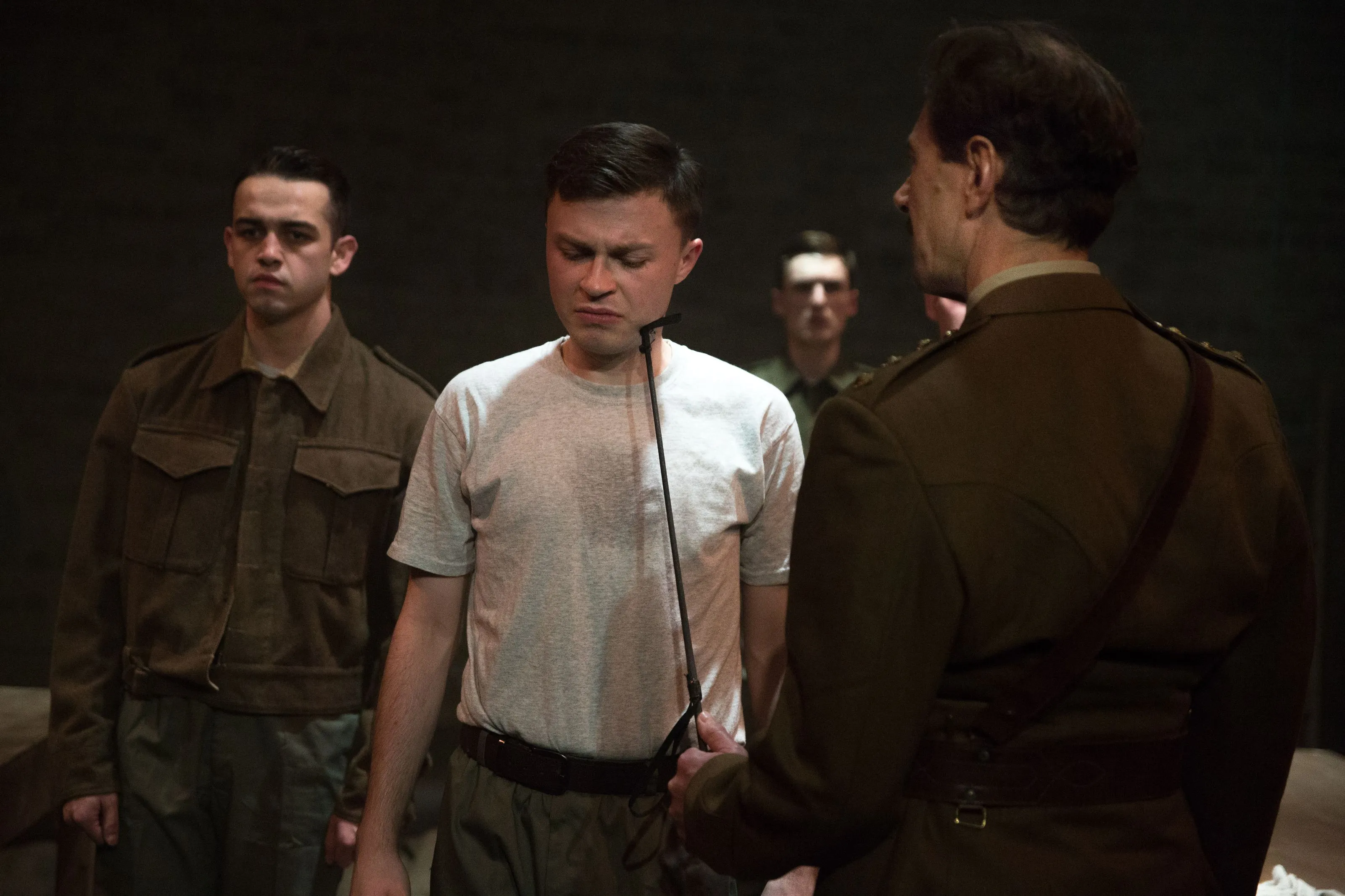 A man in military dress threatens another man with a riding crop