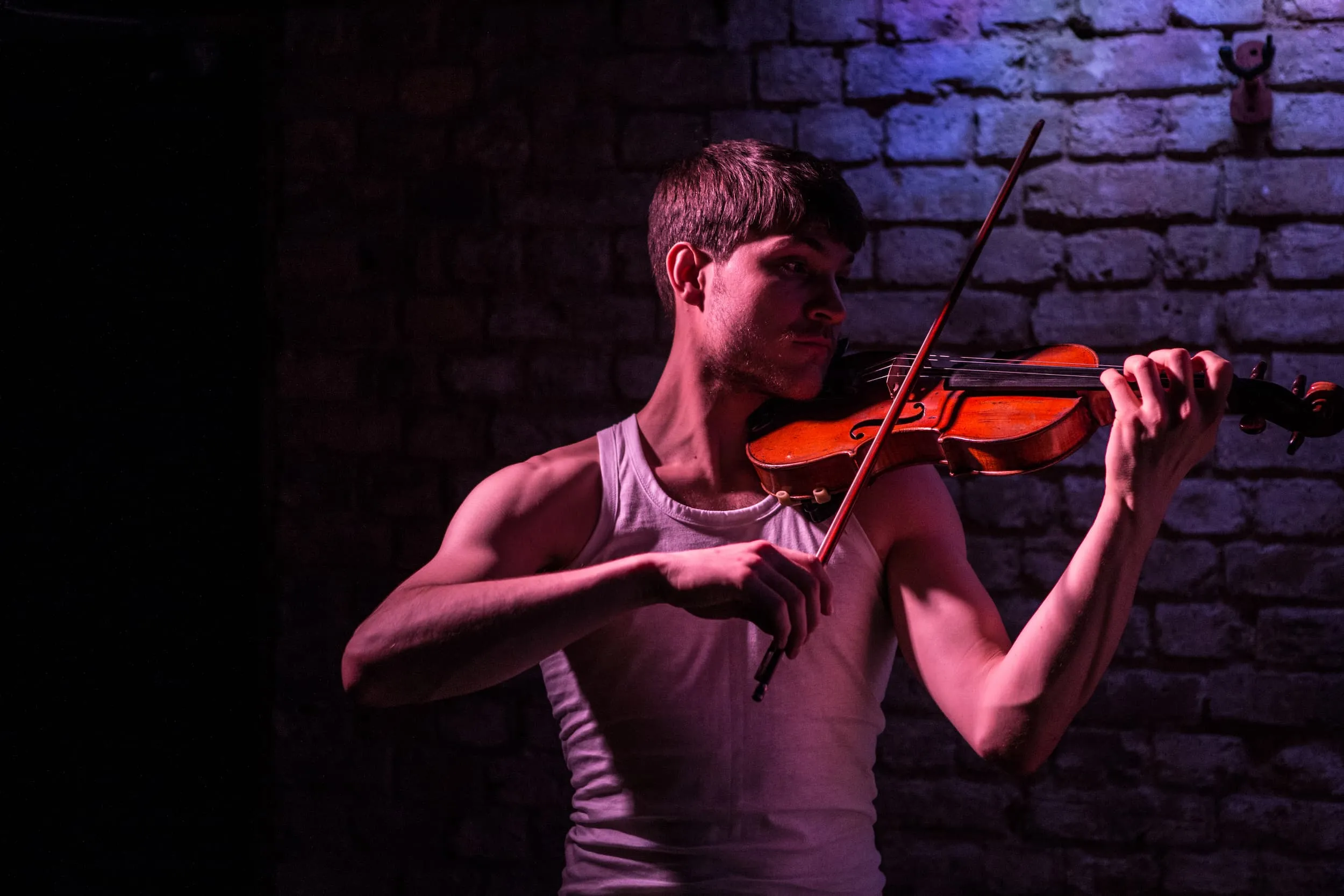 A man in a vest plays the violin in dim warm light