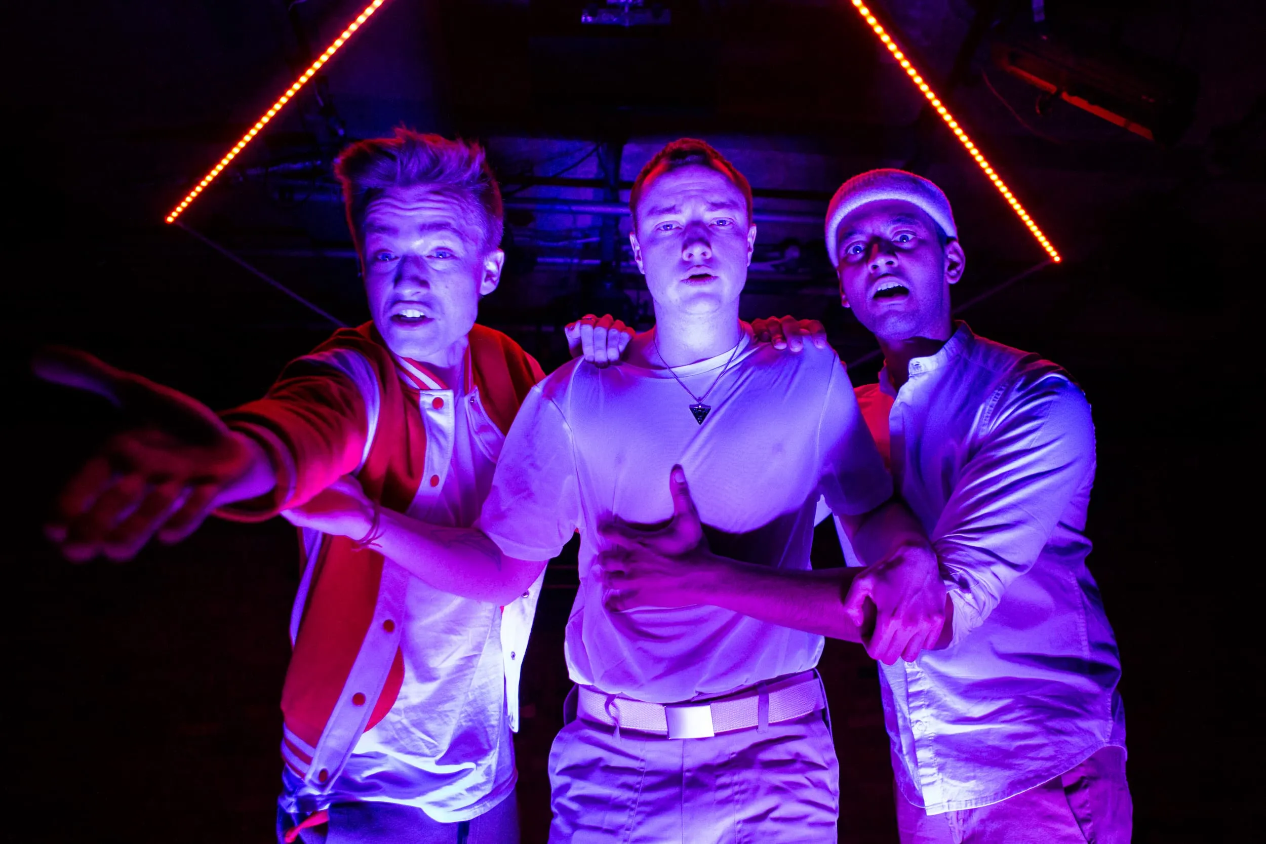 In garish neon light, three men approach the camera with wild looks on their faces