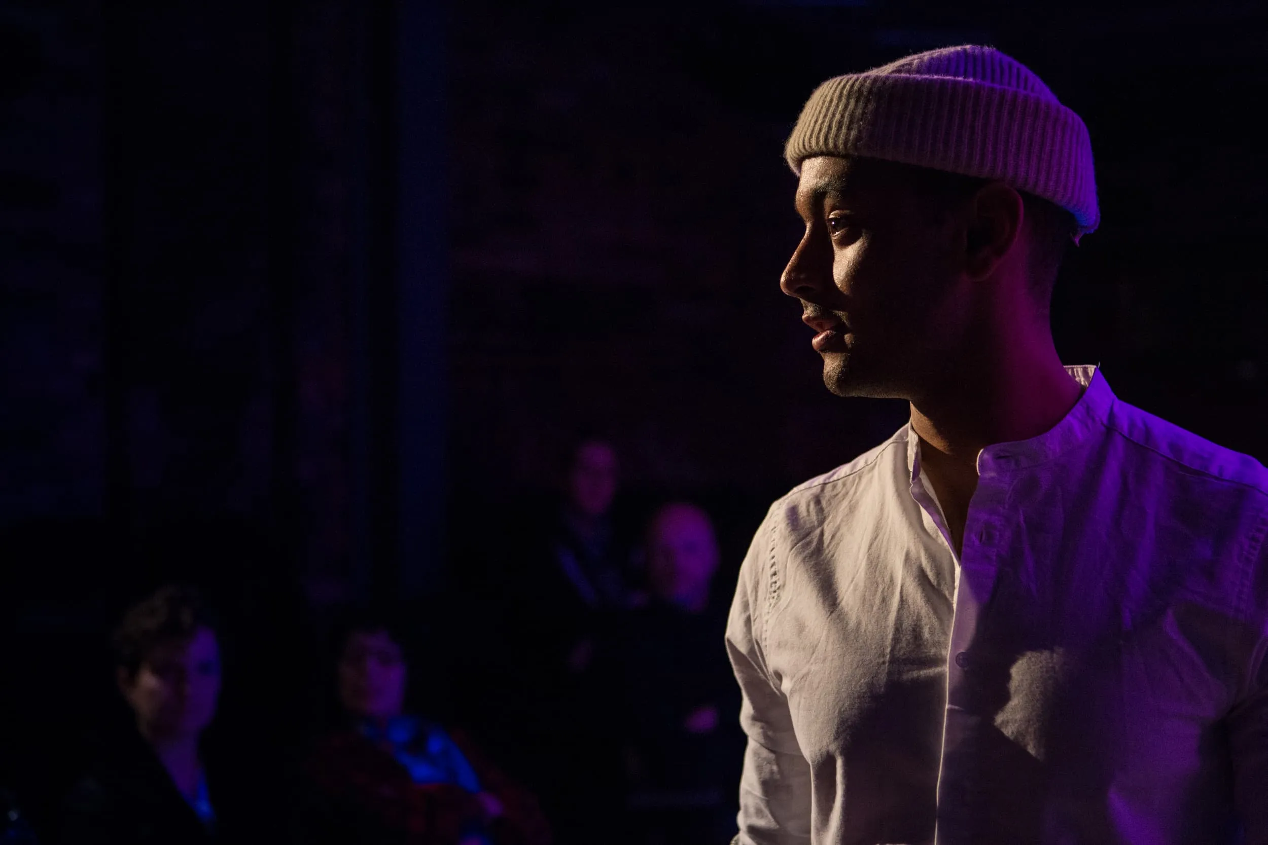 A man in a cream shirt and warm hat stares intensely into the distance with stark backlighting.