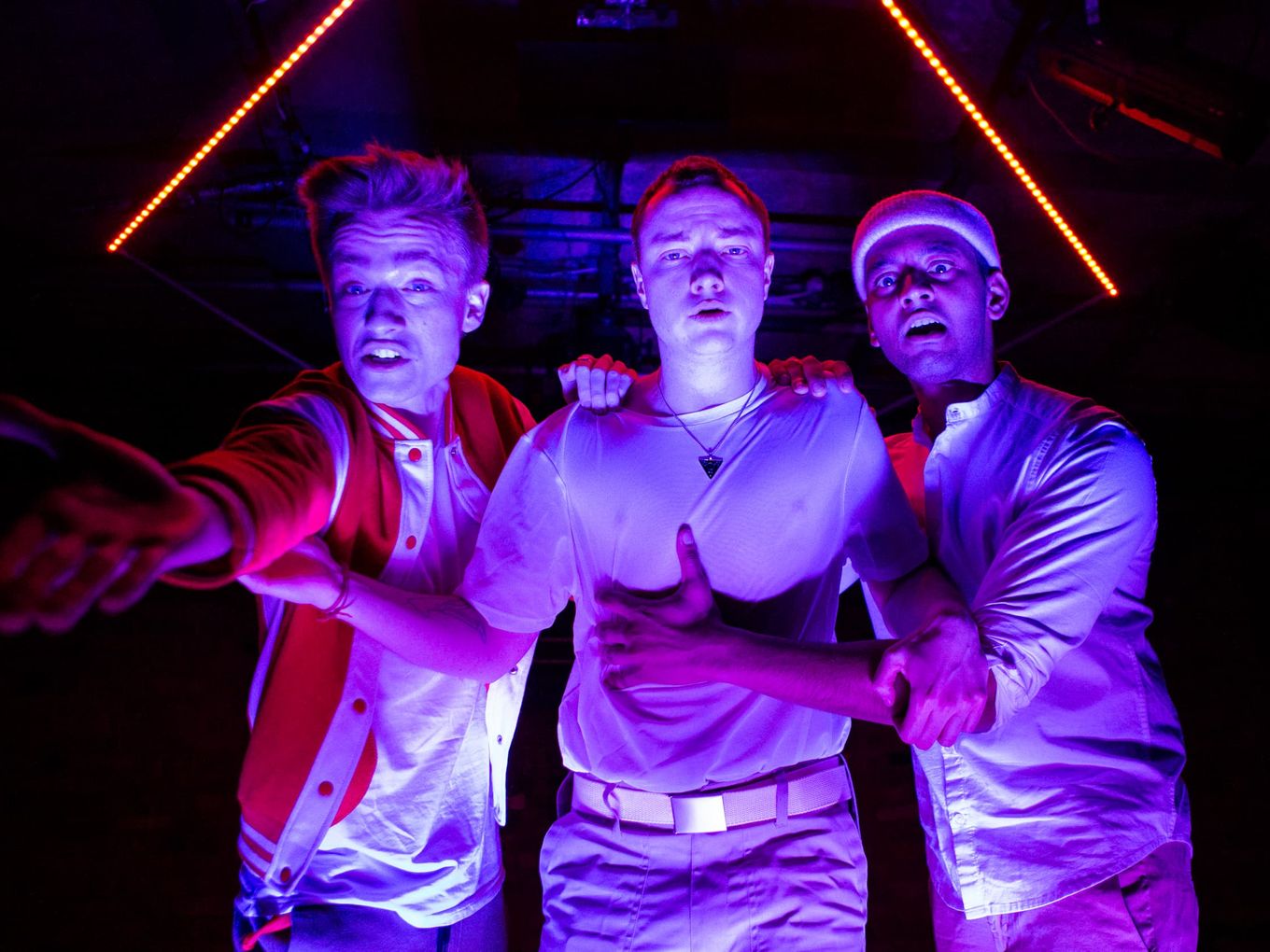 In garish neon light, three men approach the camera with wild looks on their faces